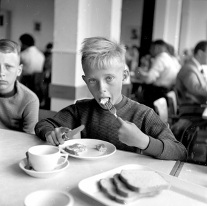841944 Afbeelding van een jongen tijdens het ontbijt in het vakantieoord Westerduin te Wijk aan Zee.